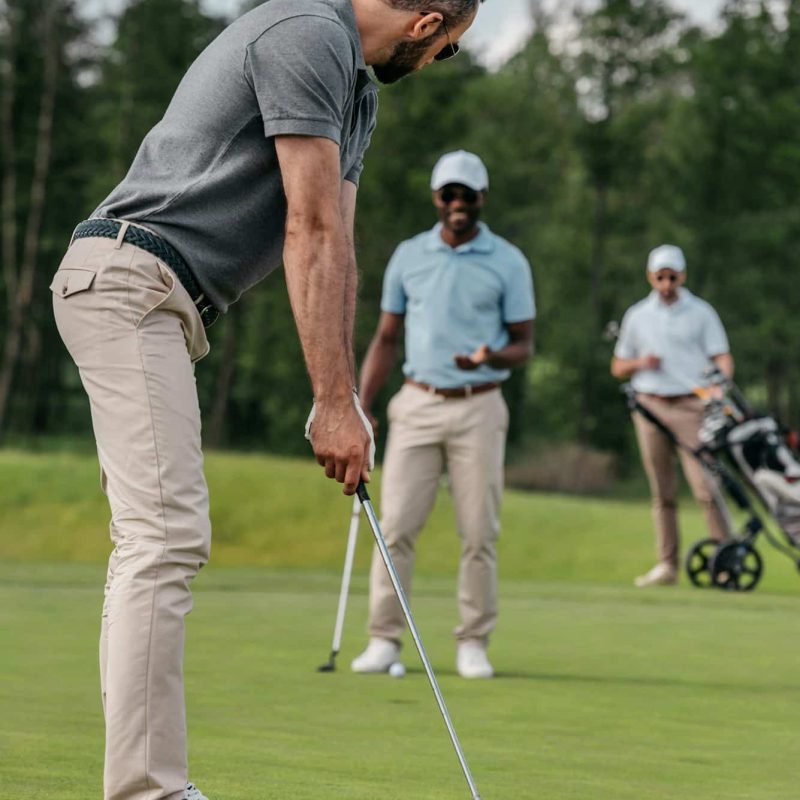 golfer aiming to hit a ball with club during play with his friends at daytime